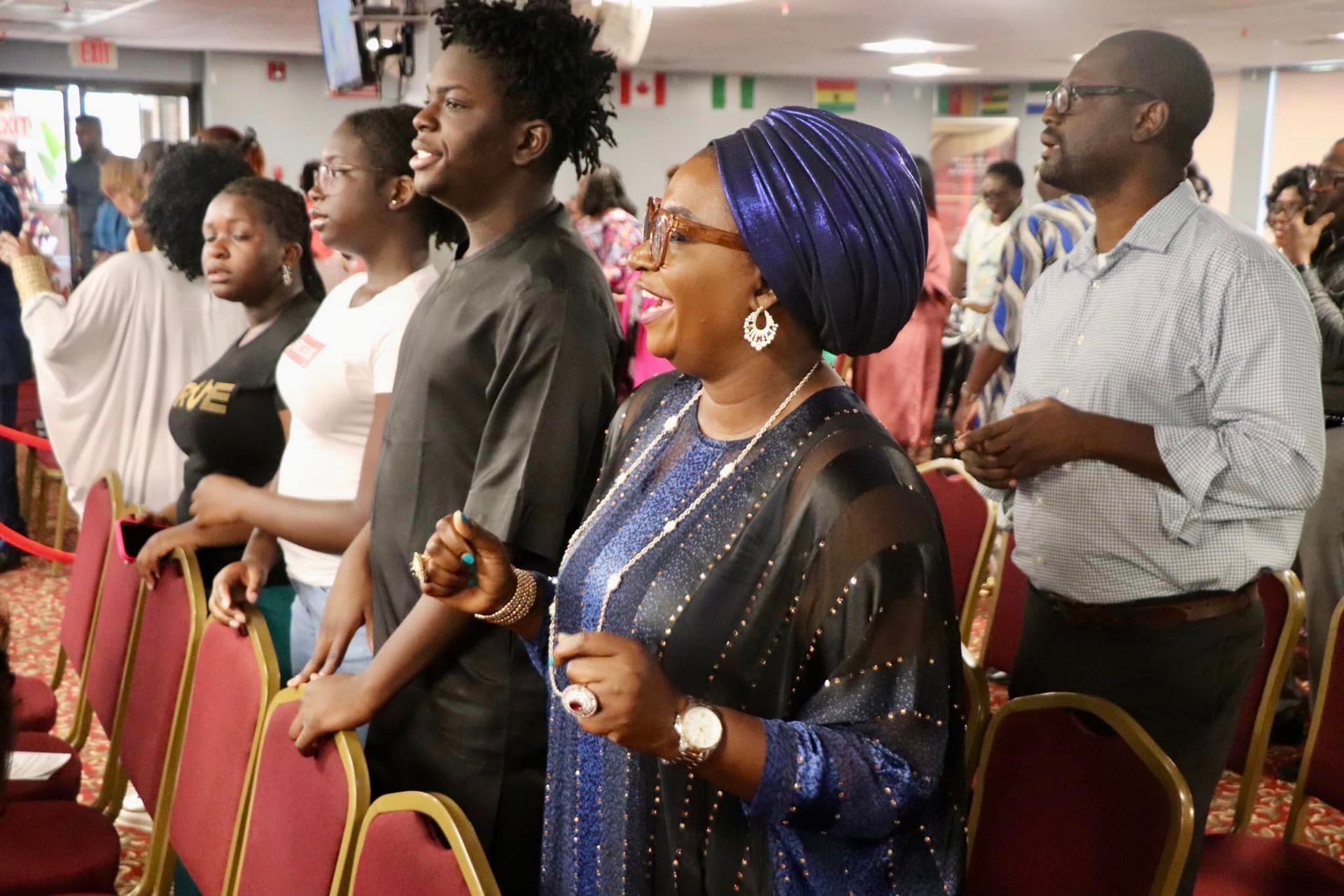 Group of people in a brightly lit room, some with arms raised, expressing joy and worship.