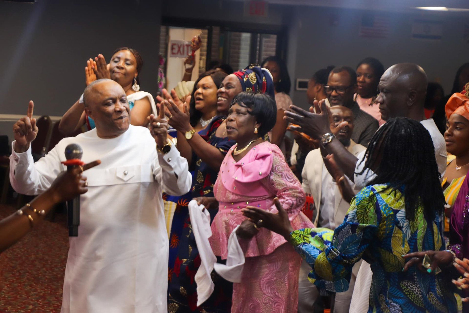 Group of people in colorful outfits, raising hands, singing, and celebrating indoors.