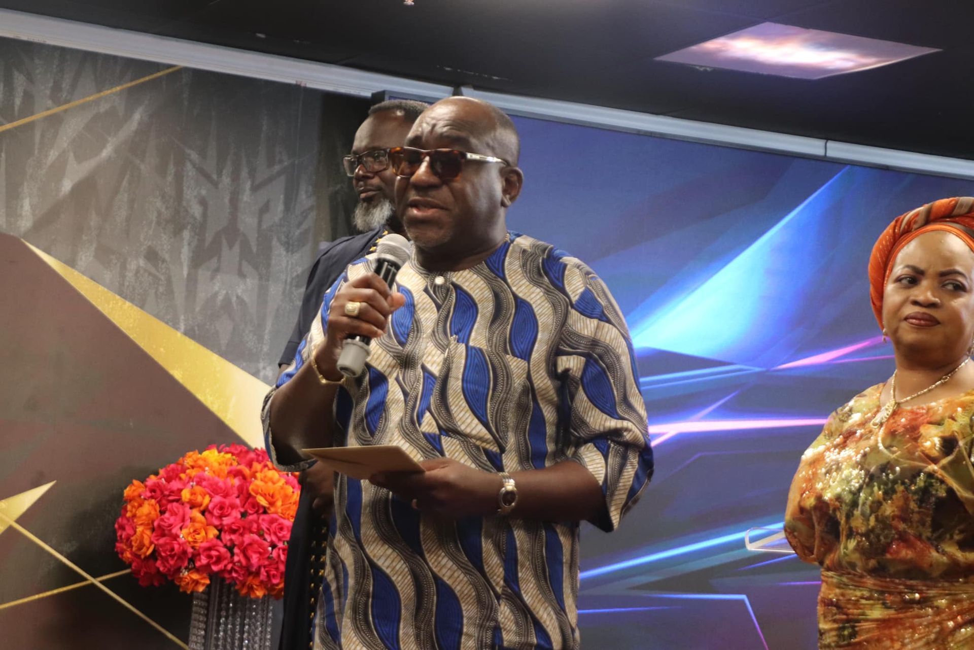 Man in patterned shirt speaking into microphone at event.