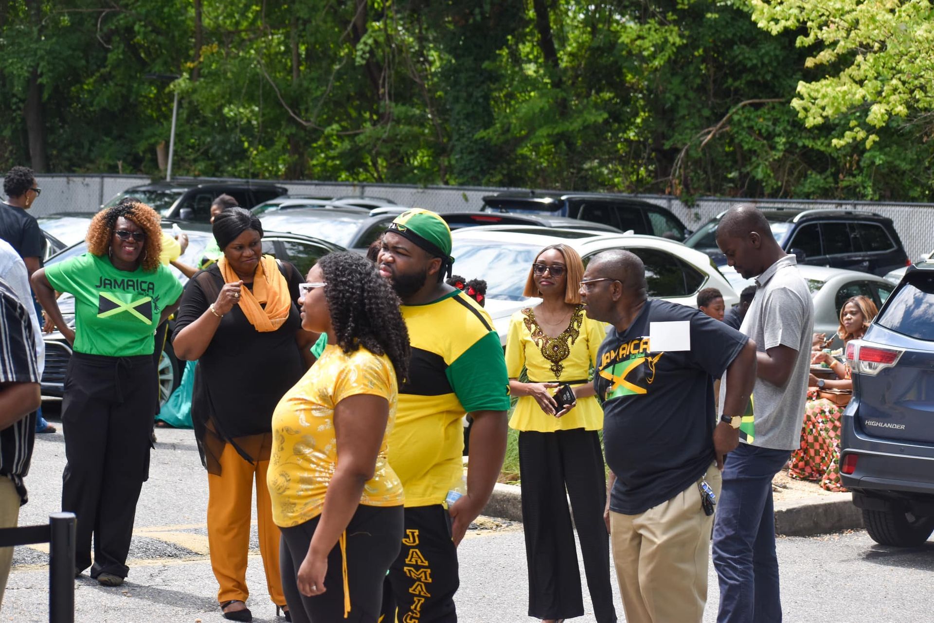 Group of people wearing Jamaican flag colors, outdoors in front of parked cars.