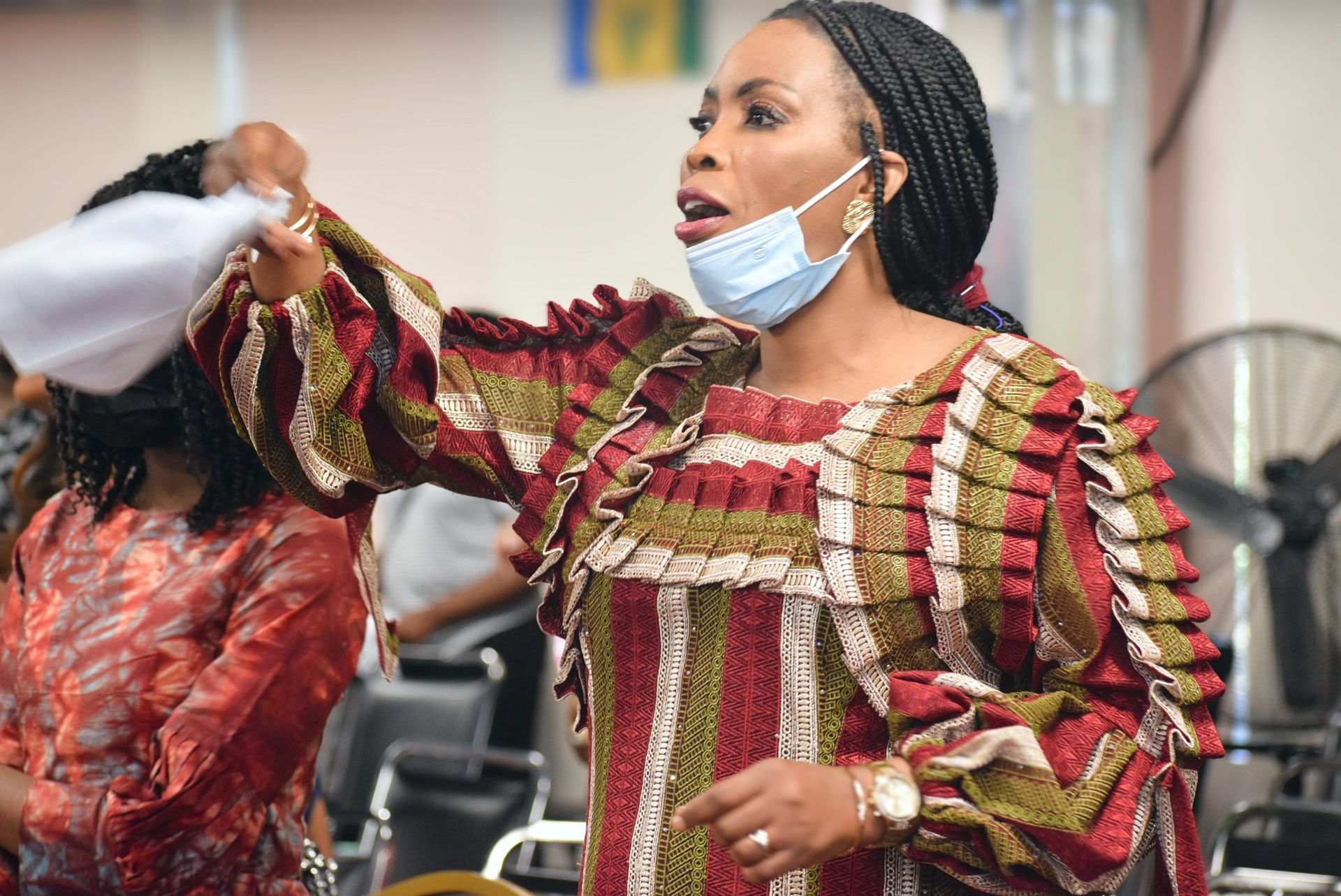 Woman in colorful dress gestures, face mask down, indoors.