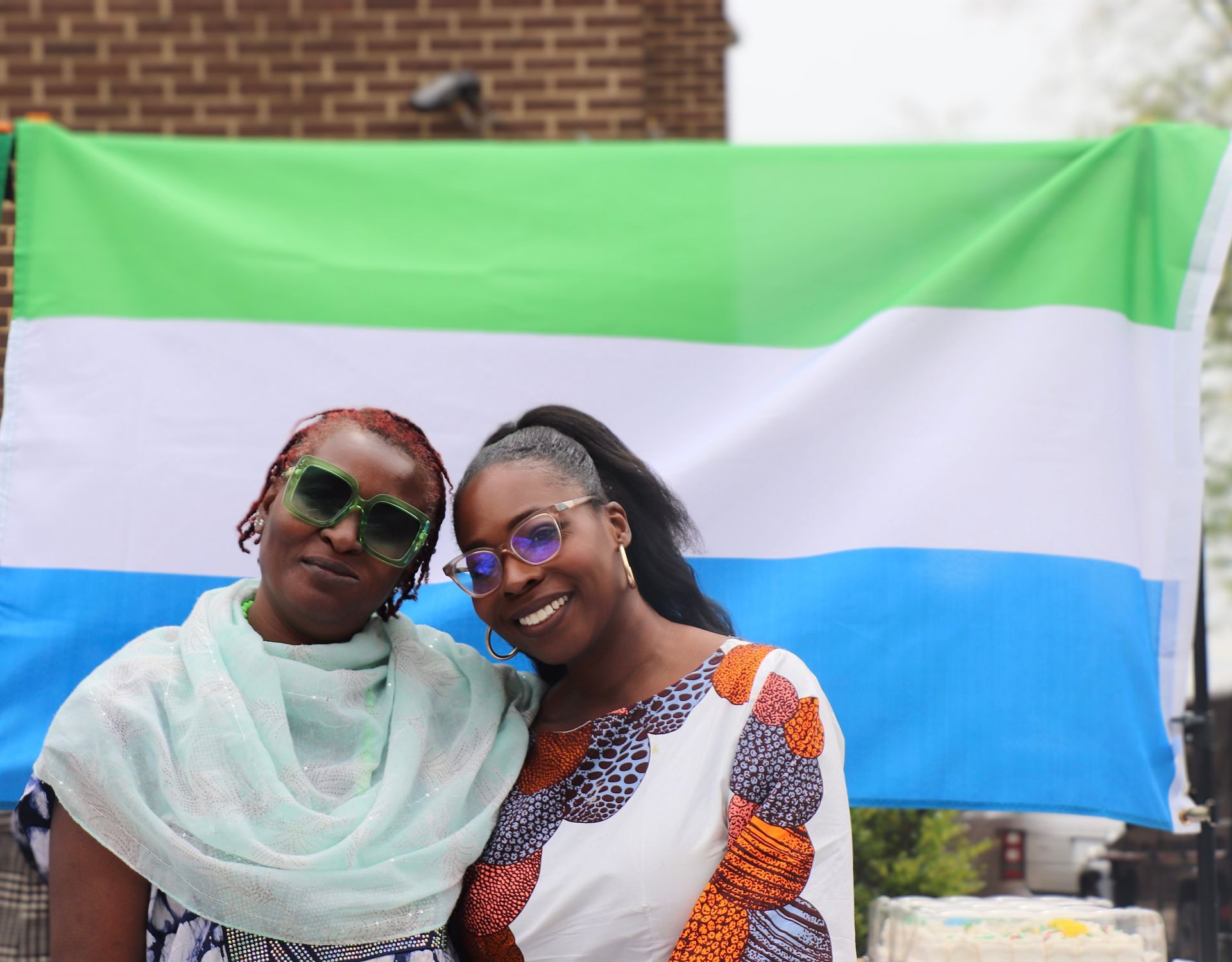 Two women smile, posed in front of Sierra Leone flag.