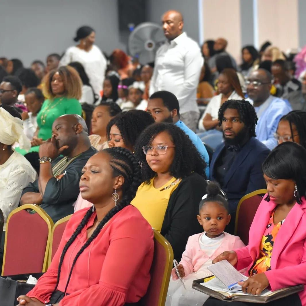 Audience in a large room, diverse group attending an event, some looking forward, listening.