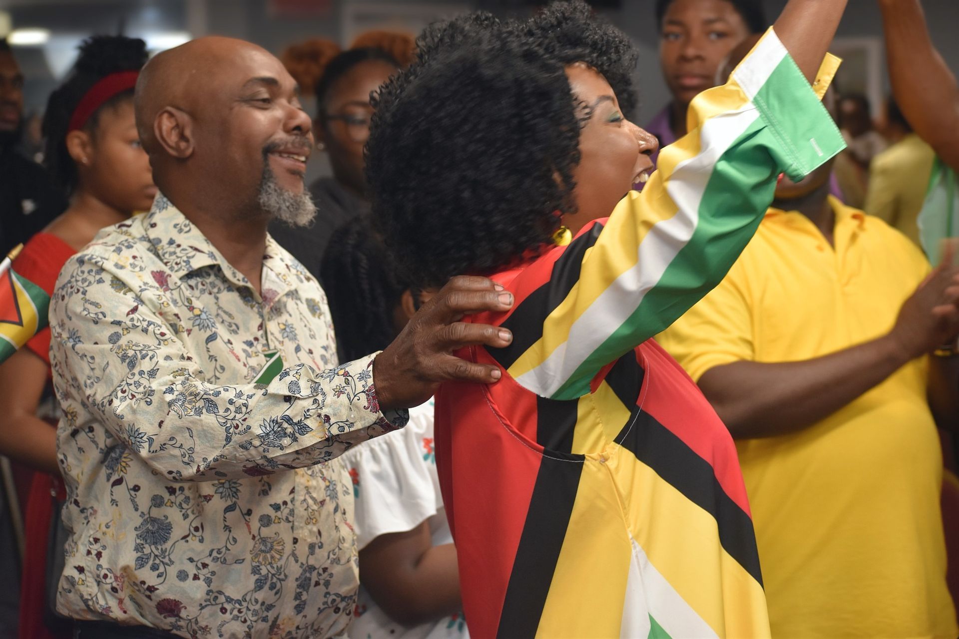 Man in patterned shirt supports woman in colorful dress, arms raised, in a crowd.
