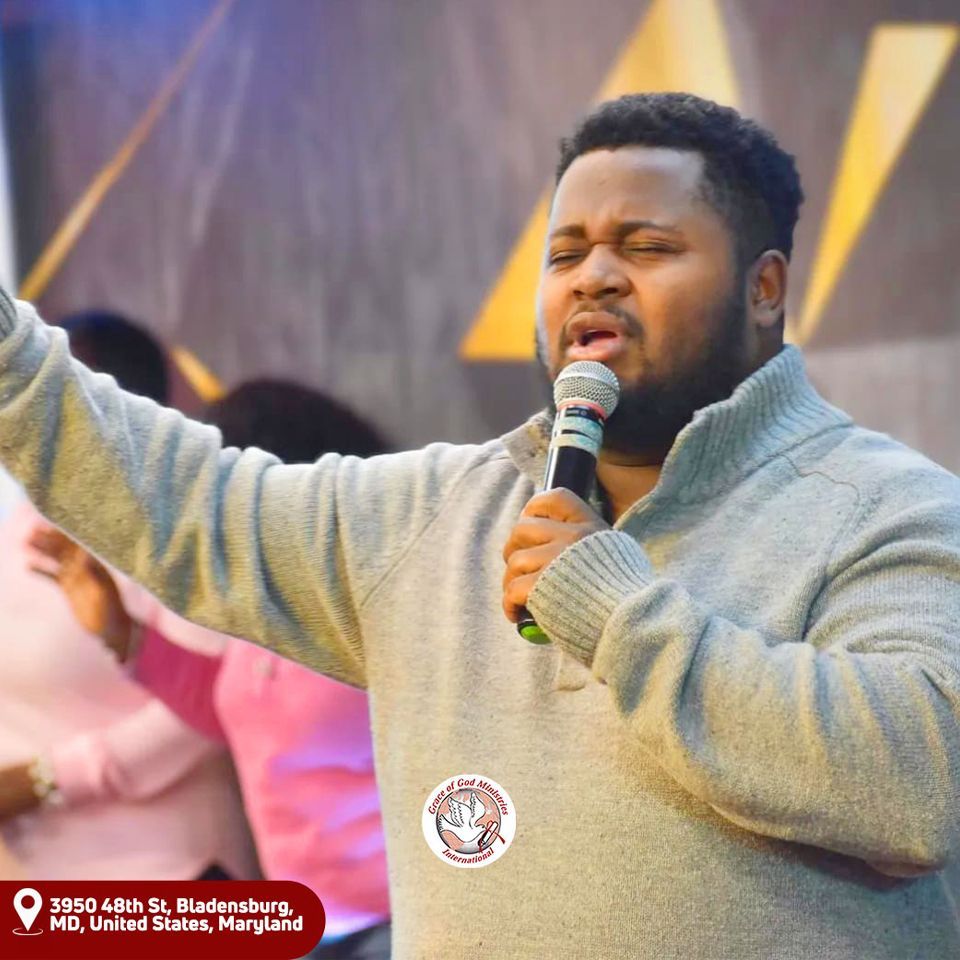 Man with microphone, eyes closed, raising hand while leading worship, located at 3950 48th St, Bladensburg, MD.