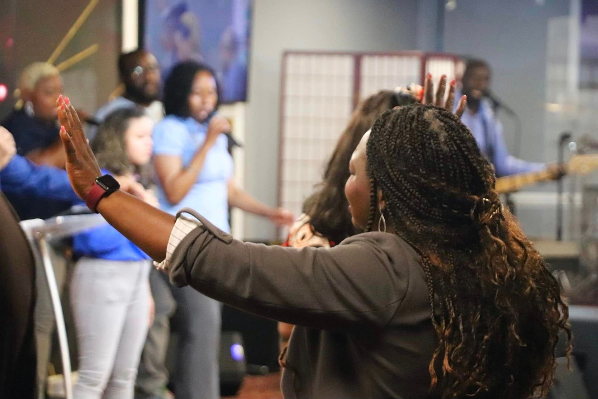Worship service with a woman raising her arms in praise, band playing, people singing and some in prayer.