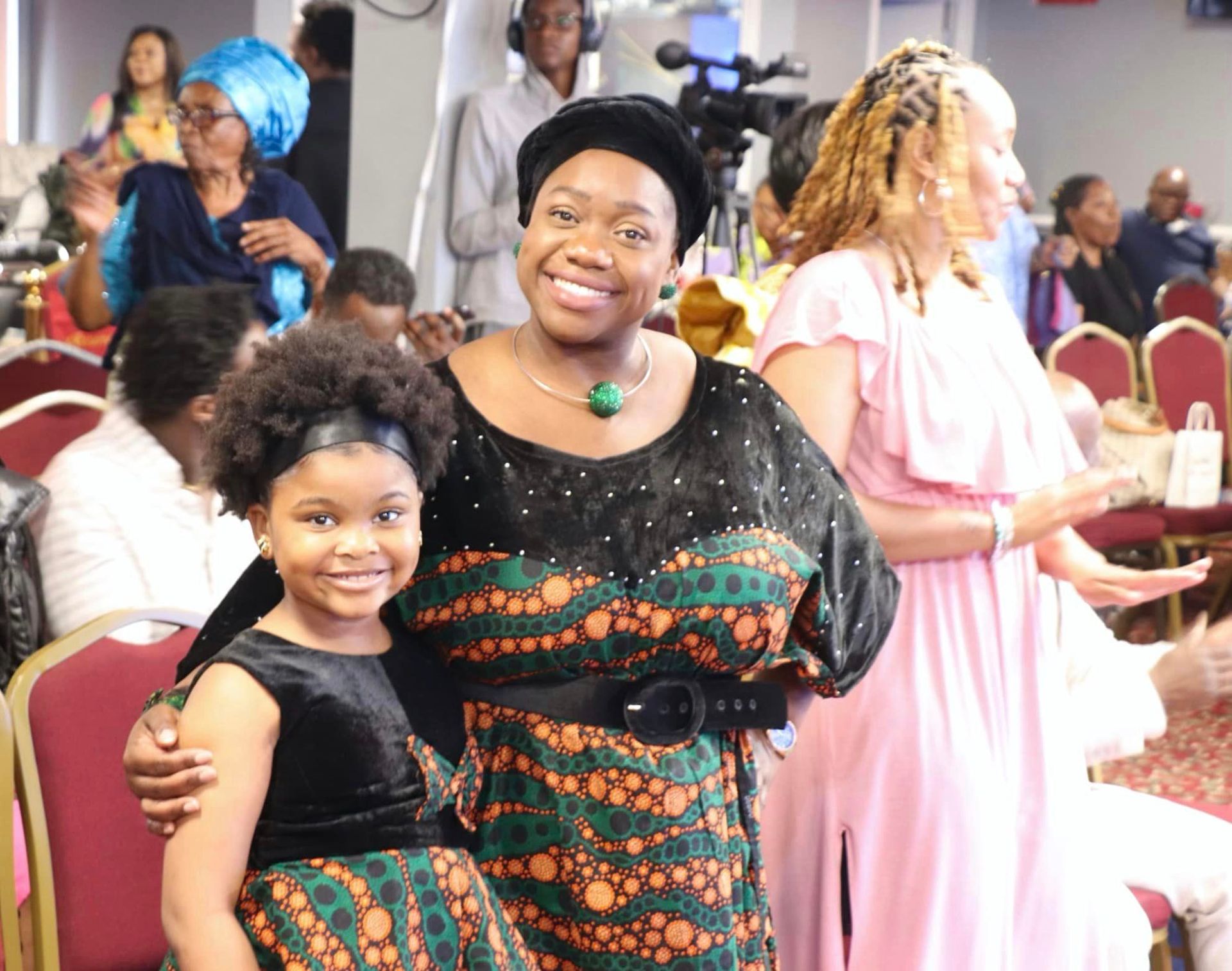 Woman and child in traditional dresses, smiling, pose with another woman at an event.