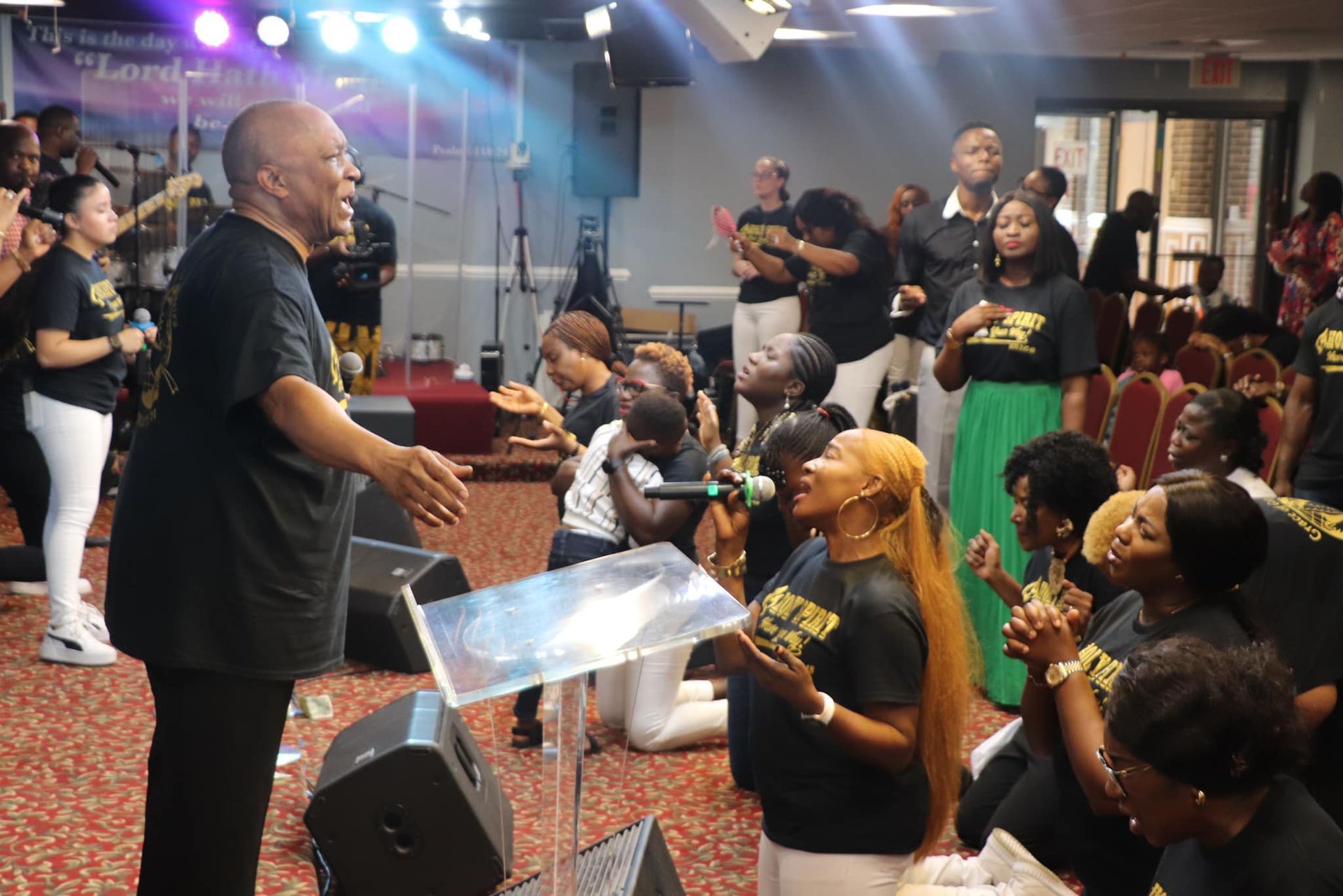 People praying and singing in a church. Group is kneeling, hands raised, and the preacher gestures.
