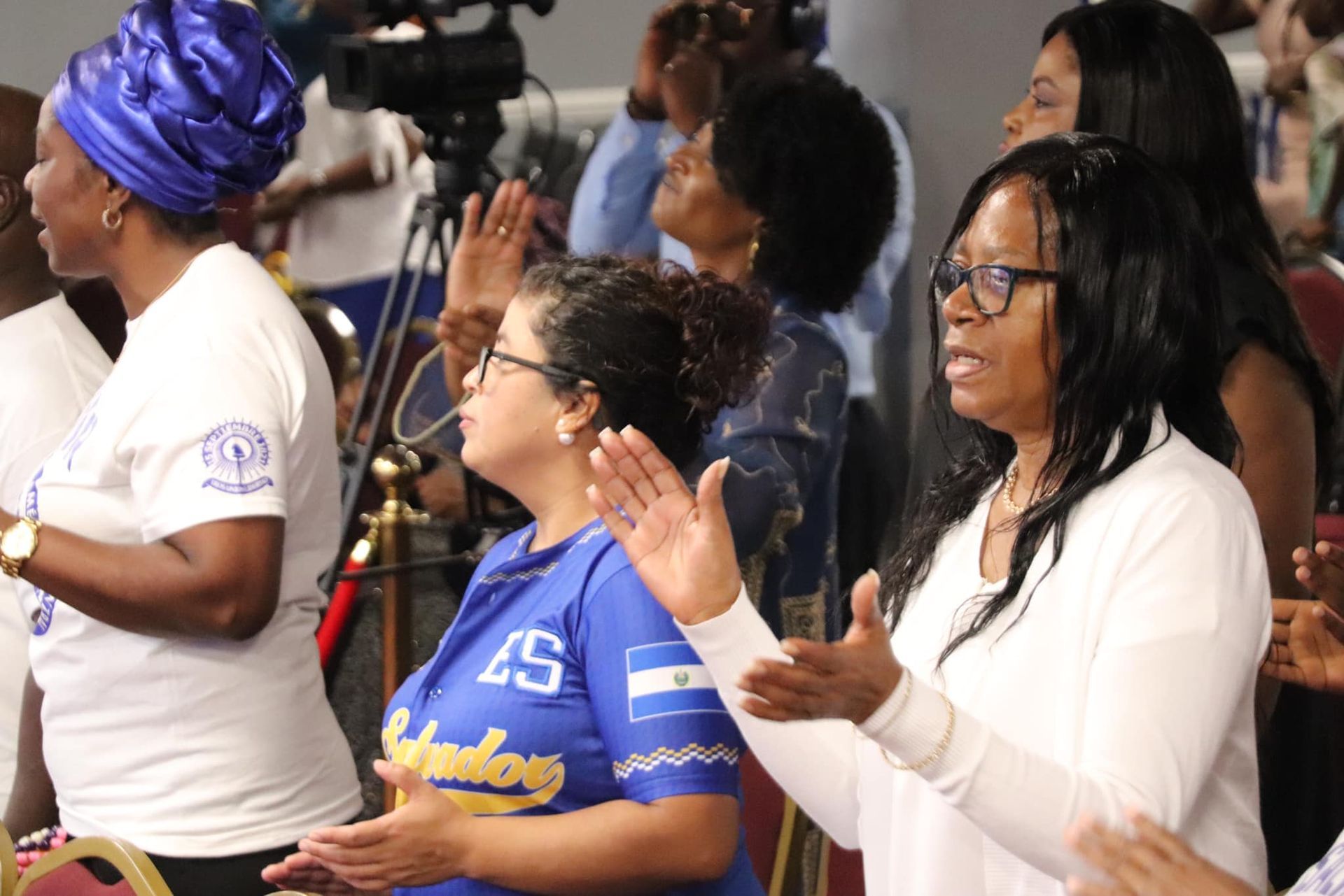 People clapping and raising hands in worship. Some are wearing white shirts.