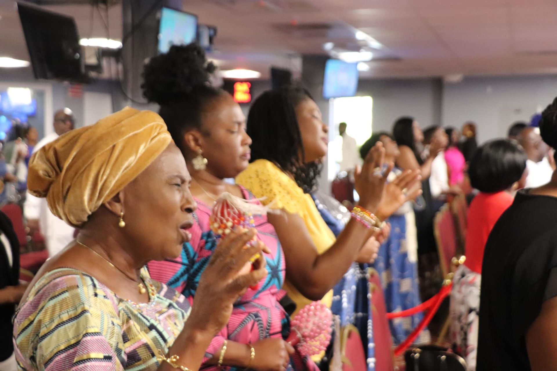 People in a church raising hands in prayer, with a woman in the foreground wearing a headwrap.