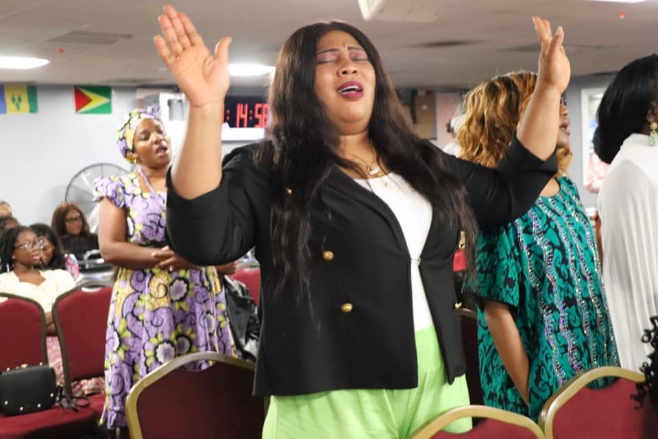 Woman with arms raised in worship at a church service. Other attendees stand in the background.