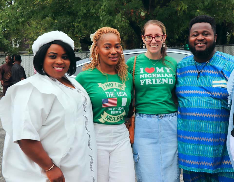 Group of people smiling, wearing green shirts and Nigerian attire outdoors.