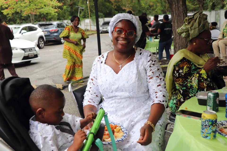 Woman in white dress smiles with a child. Outdoor event.