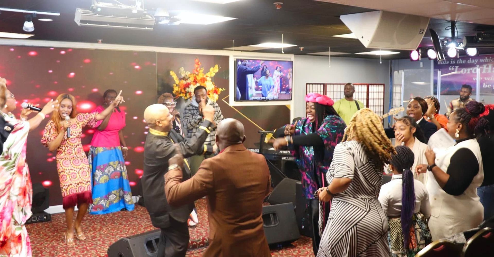 People dancing and singing in a church. A screen in the background shows a performance.