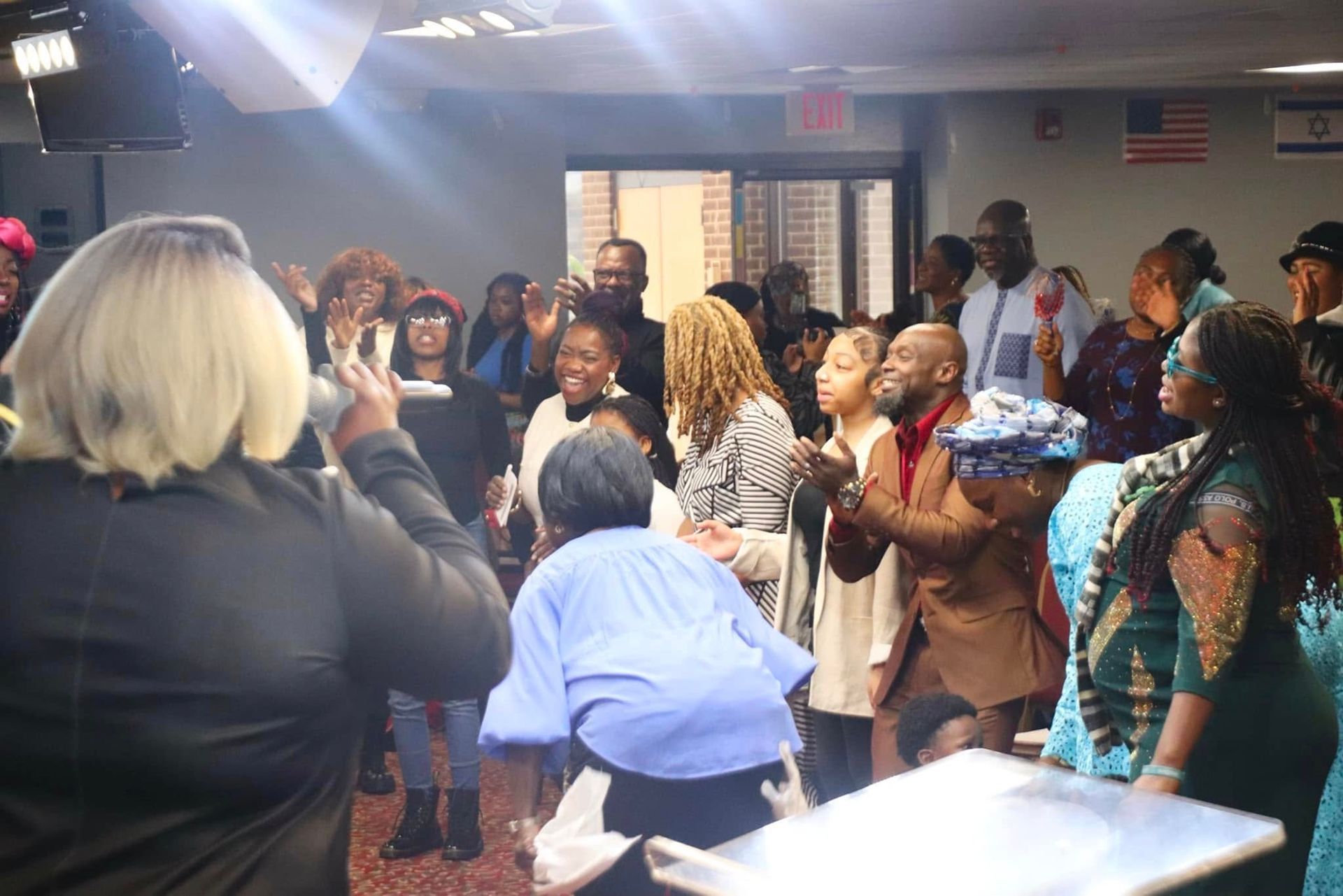 Group of people celebrating joyfully in a room with an American flag; some are clapping.