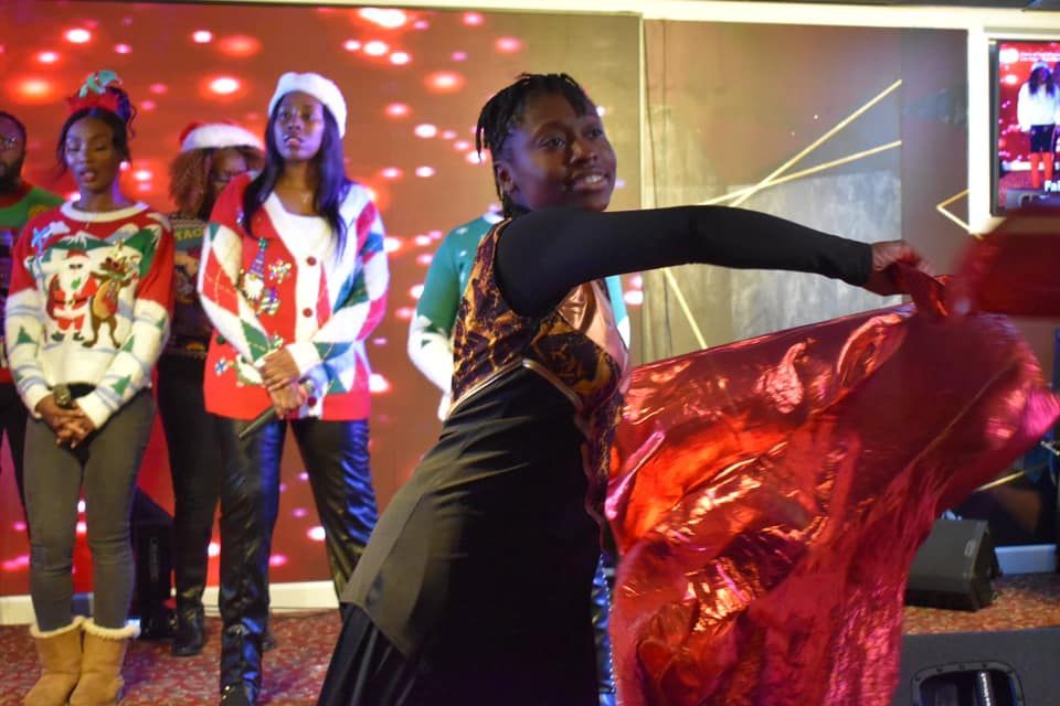 Woman in black dress waving a red cloth, with others in holiday sweaters and Santa hats.