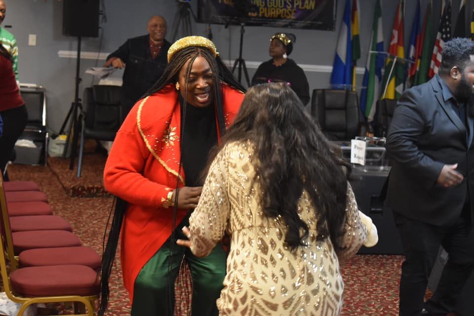 Two people dancing, a man in red and woman in gold, at an event with flags in the background.