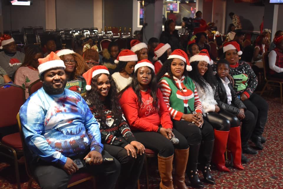 Group of people wearing Santa hats and sweaters, seated in a room. Festive Christmas event.