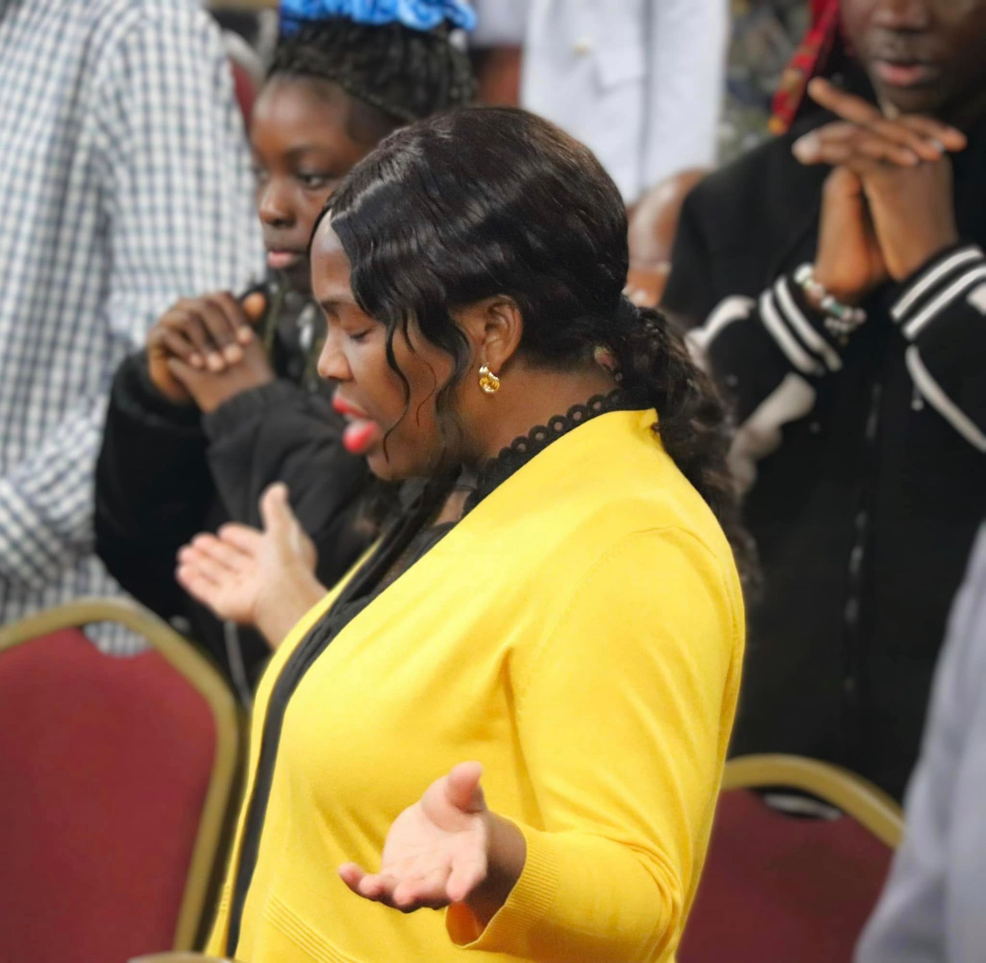 Woman in yellow praying with others at an event.