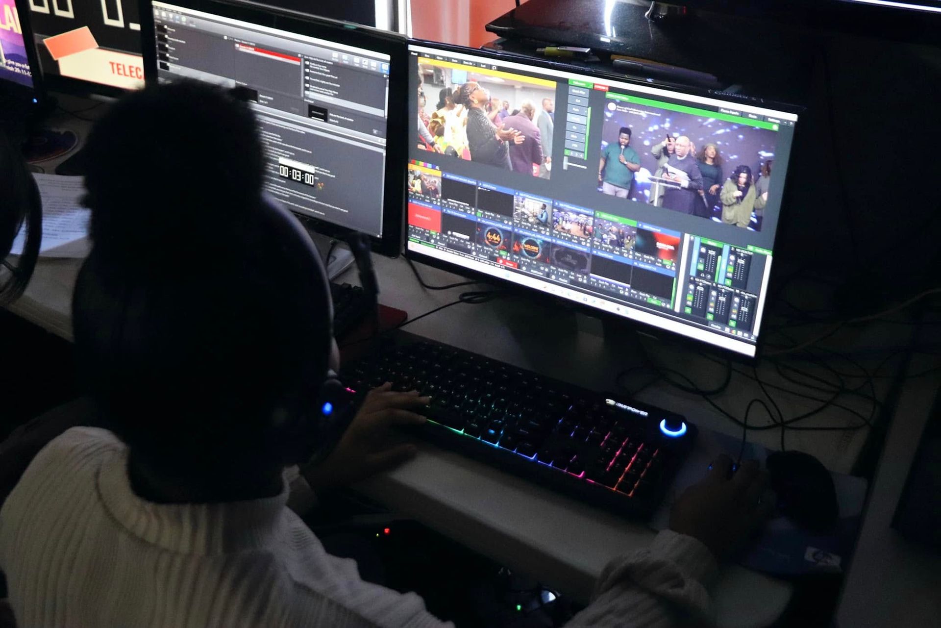 Person at a computer editing video, using keyboard with multi-screen display in a dark studio.