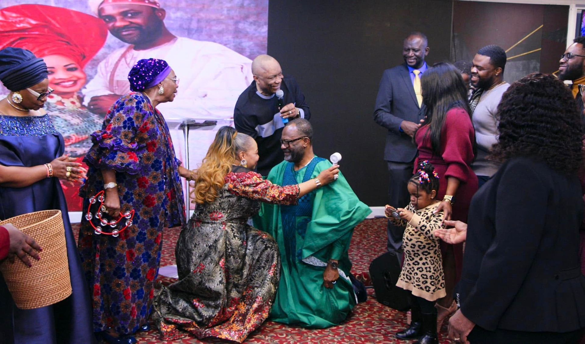 Group in colorful attire celebrates with embrace; man in green kneels.