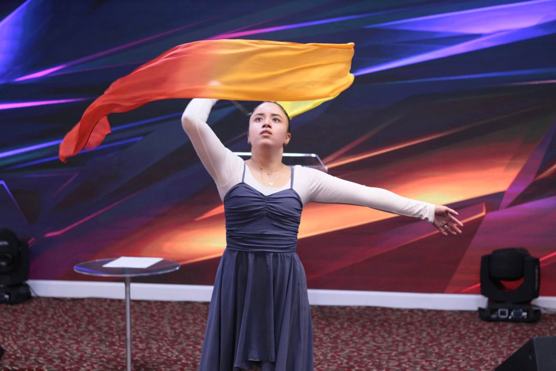 Woman dancing with a flowing orange and yellow flag, stage background.