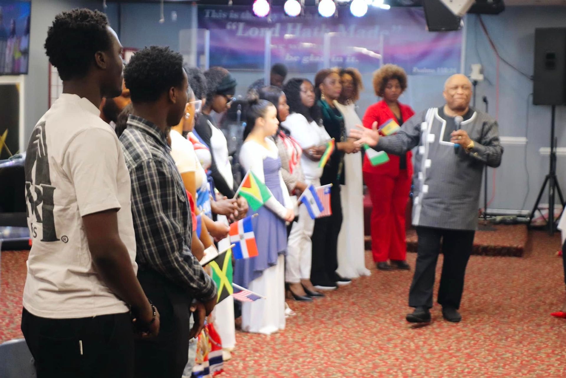 Group of people, flags in hand, listening to a man speaking in a church setting.