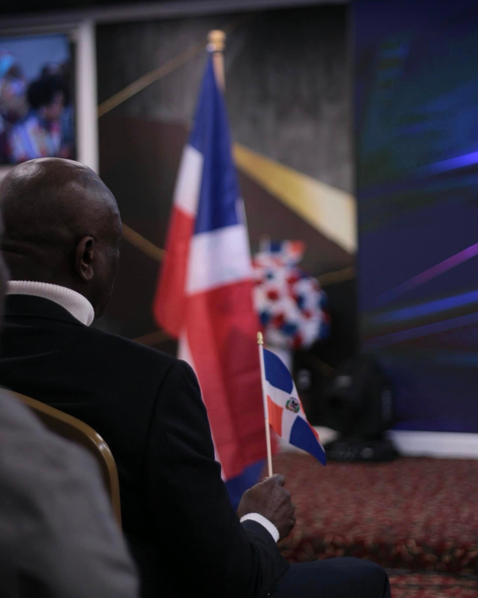 Man holding Dominican Republic flag, watching a presentation with a French flag in the background.