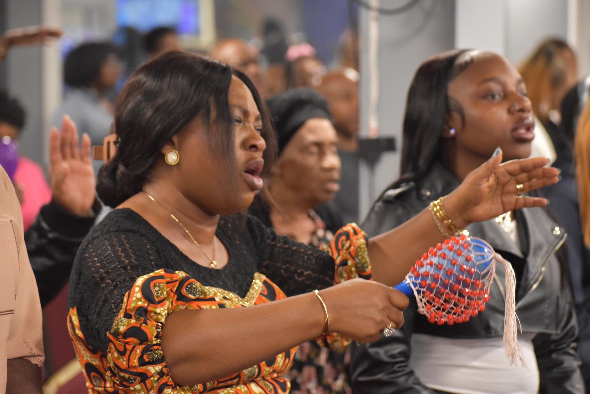 People in a church service, singing and raising hands; woman with maraca.