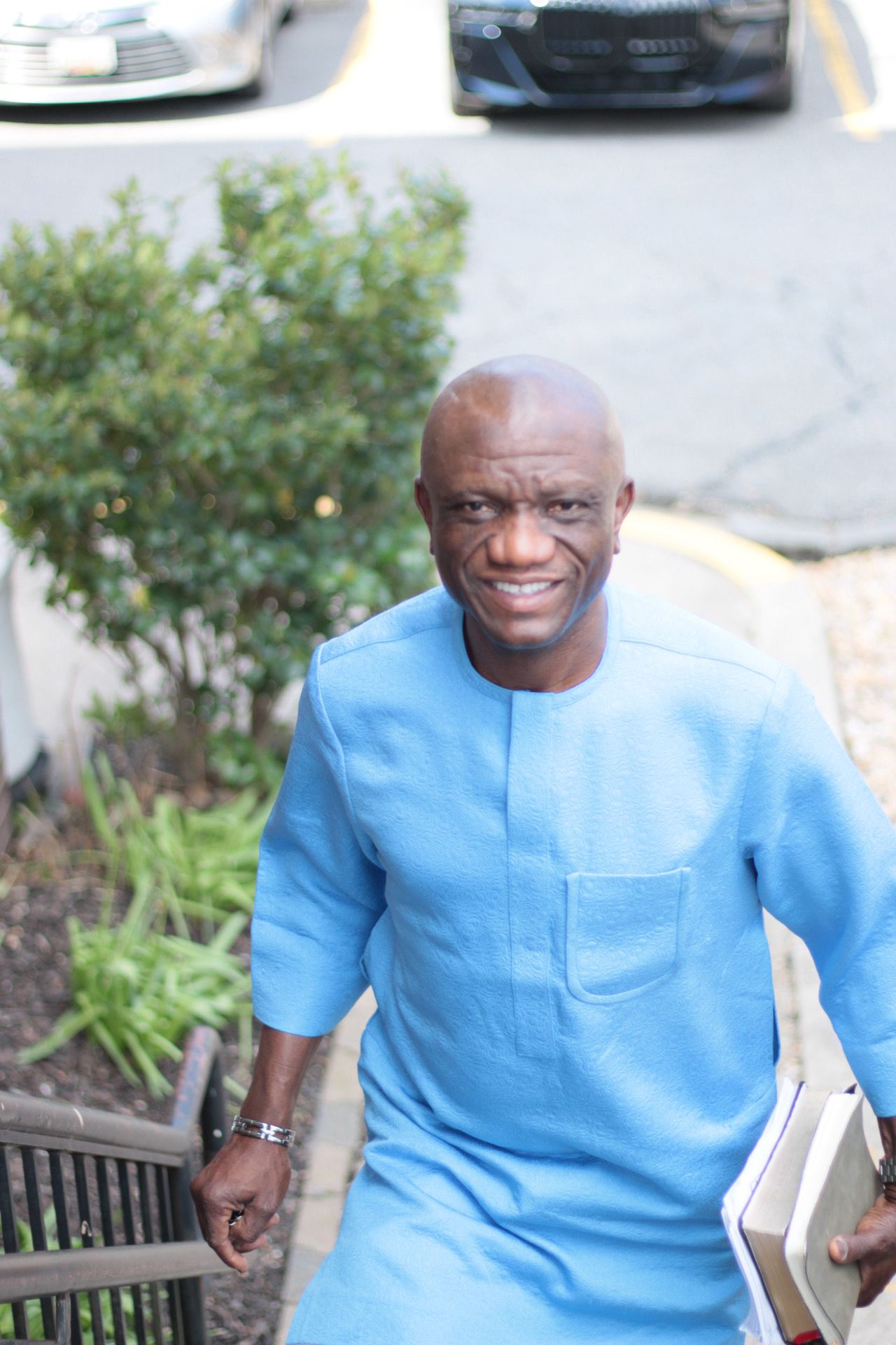Man in blue shirt climbing stairs, smiling, holding books outside.