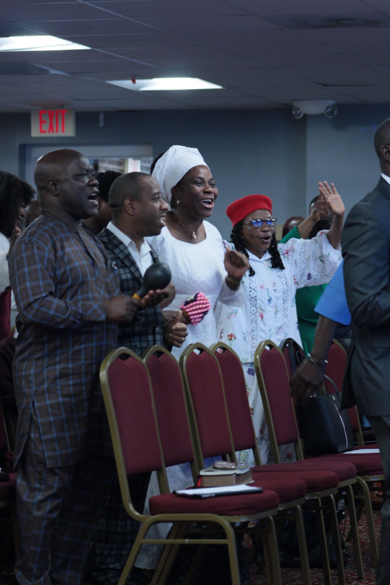 People singing joyfully in a church setting. Some wear white outfits, raising hands.