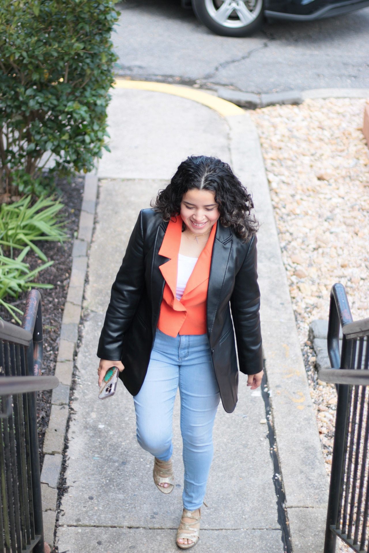 Woman in black jacket and orange top walks up stairs, smiling.