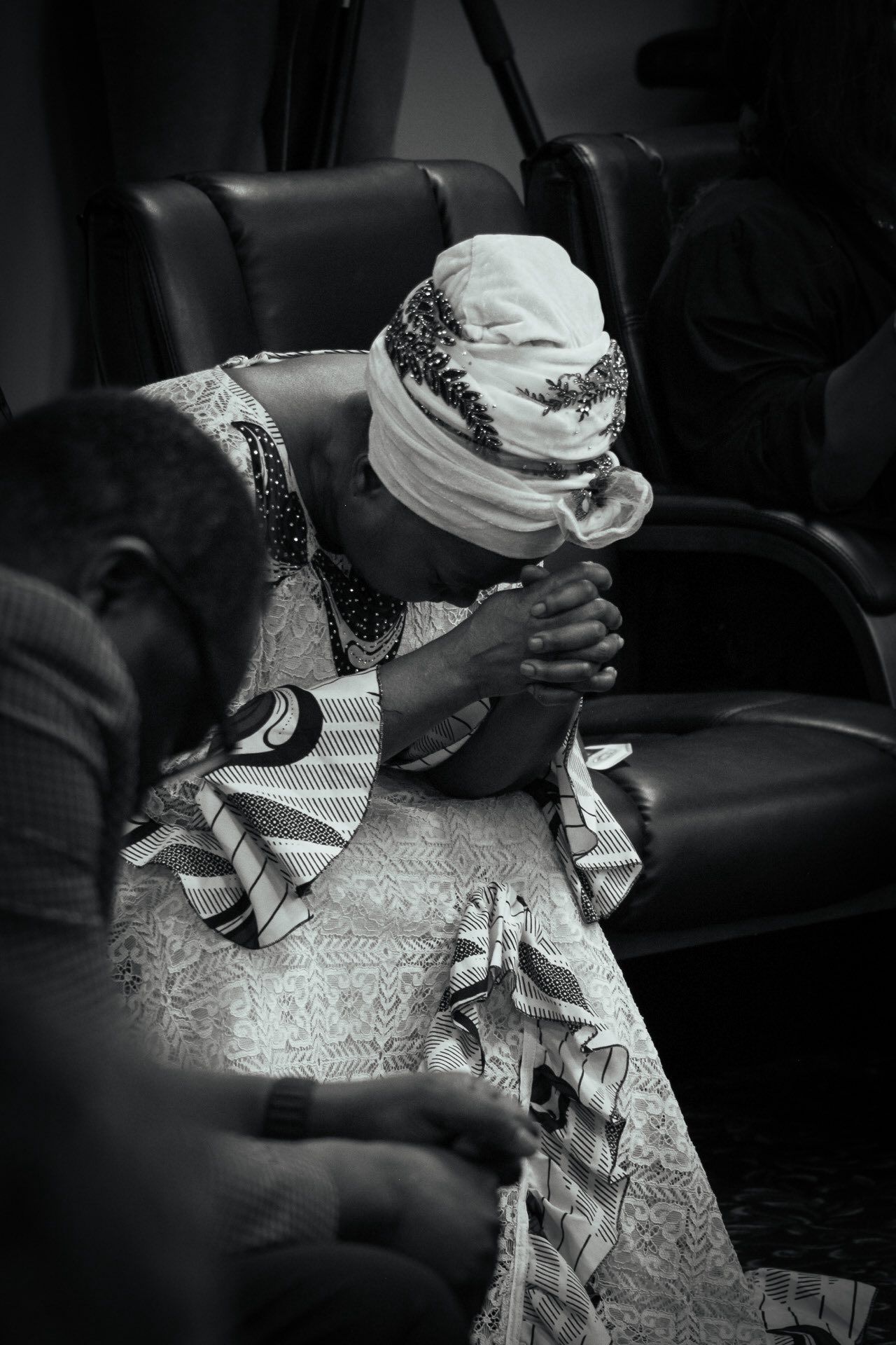Woman with headscarf prays with hands clasped, seated indoors.