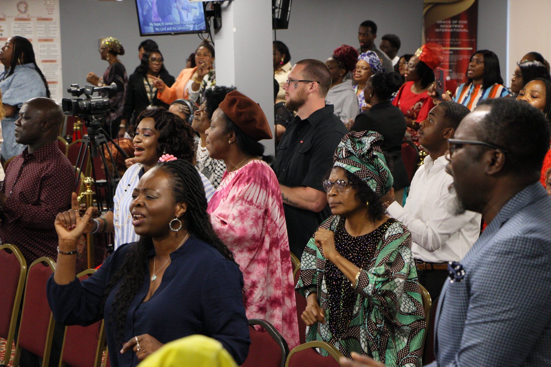 People singing and raising hands in a church service. Various skin tones, colors, and expressions.