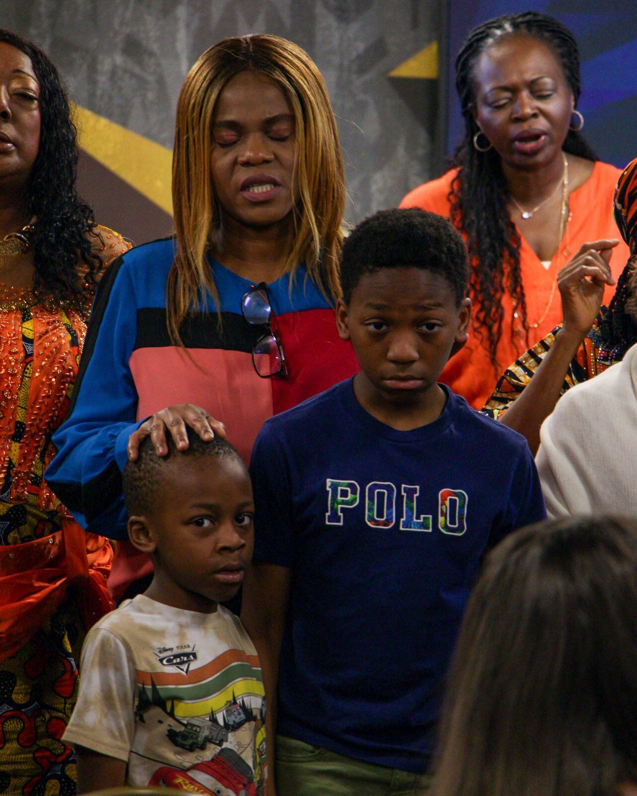 People, including two boys, in a gathering. Some appear to be praying.