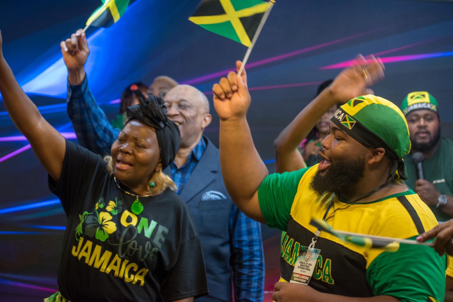 People celebrating, waving Jamaican flags, wearing green and yellow, singing.