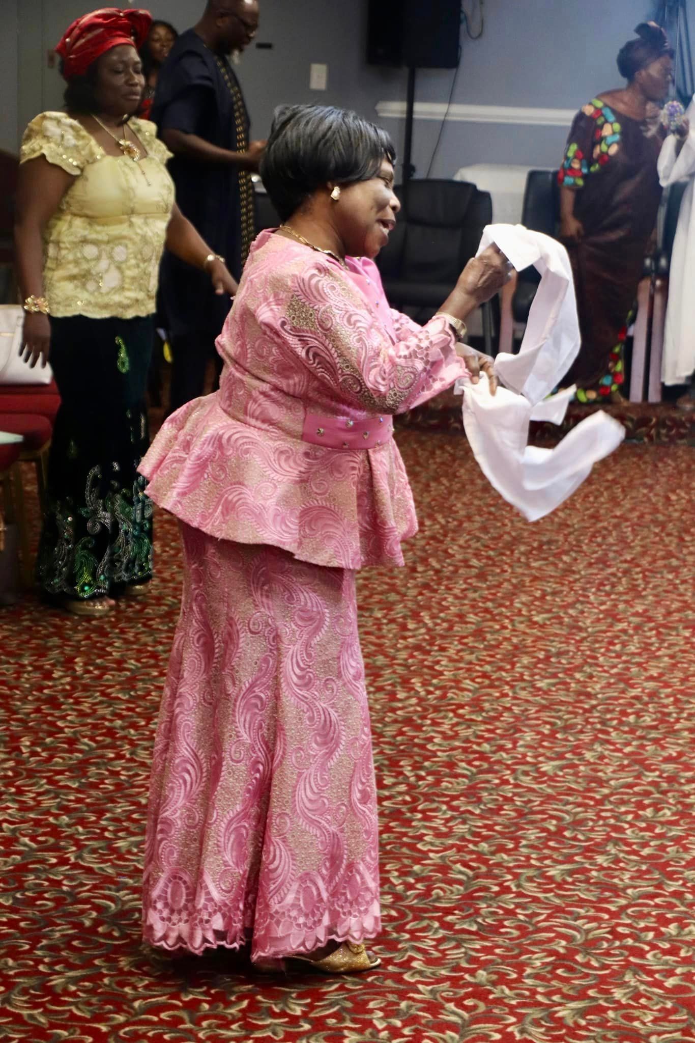 Woman in pink lace outfit waving a white cloth, in a hall with others.