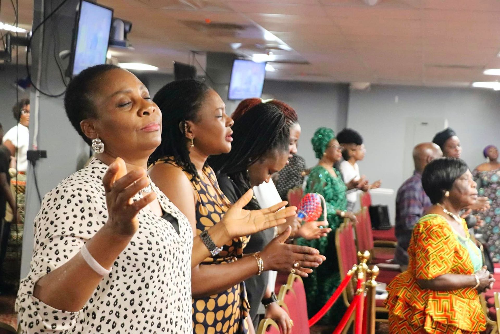 People in a church clapping, singing, and praying. Interior shot with red rope and seats.