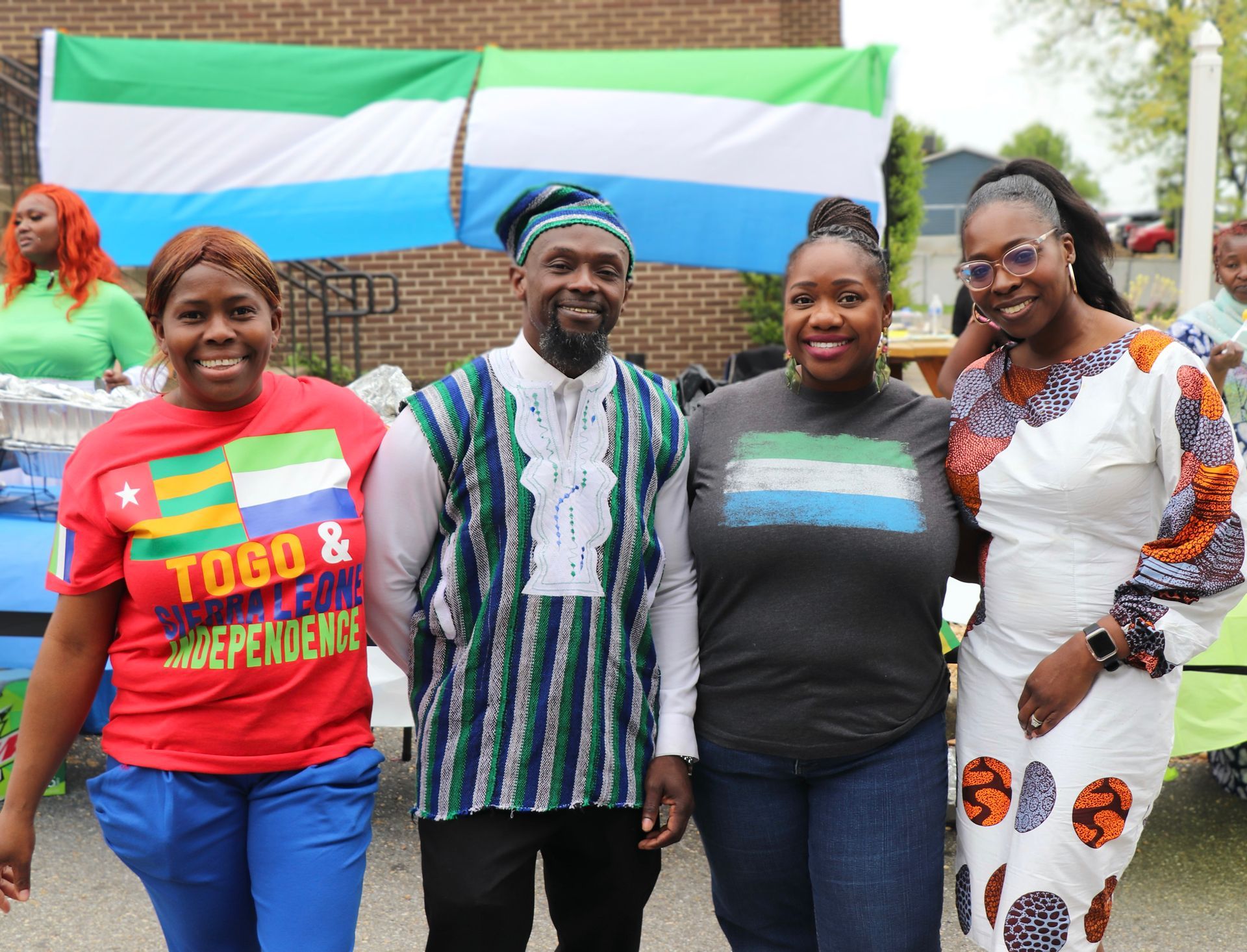 Group of people smiling, celebrating in front of a flag. One person in Togolese shirt.