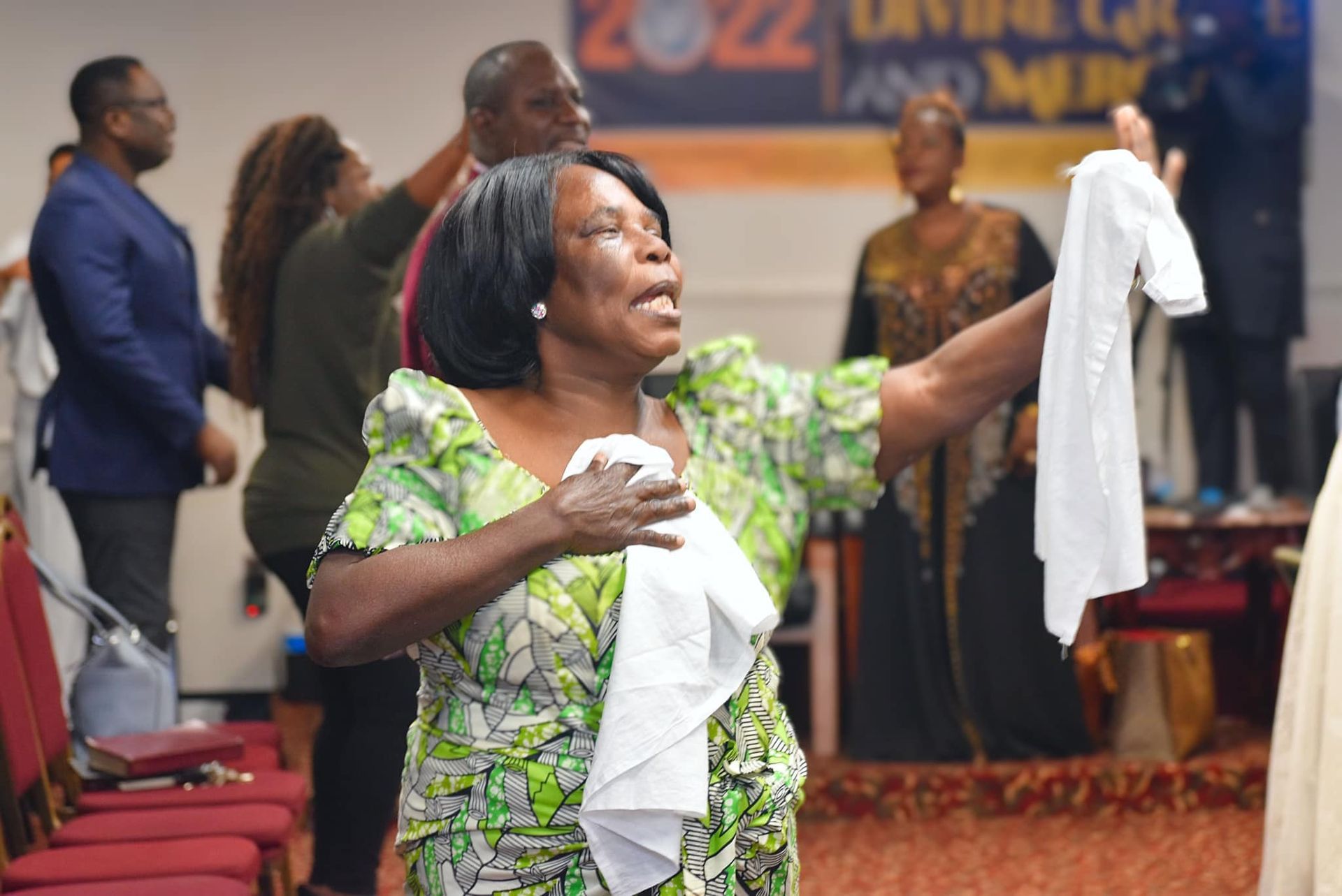 Woman in green dress raising a white cloth in a church, others around her praying.