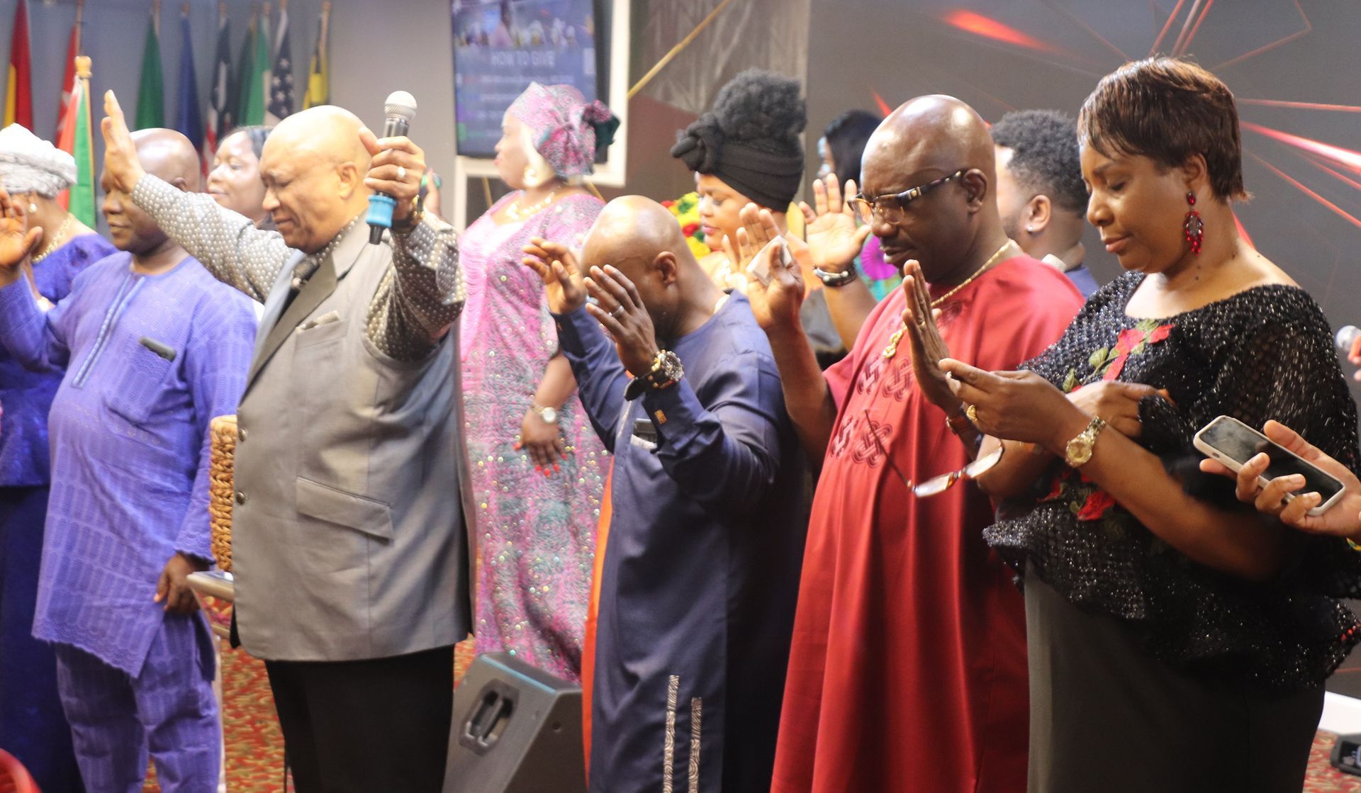 People in a church praying with raised hands. Stage with banners, focus on prayer and worship.