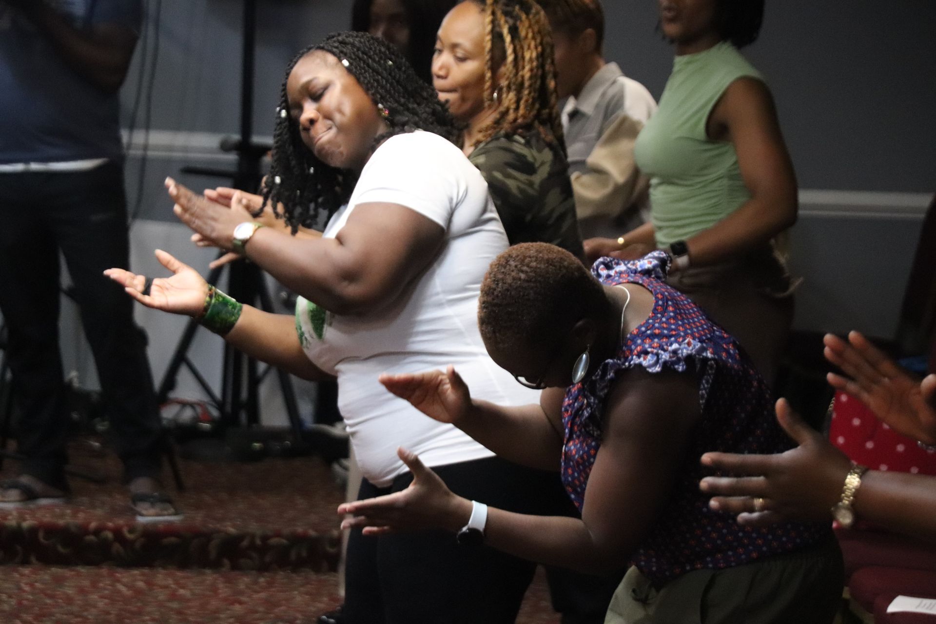 People in a room clapping and worshiping, some with eyes closed and hands raised in a church.