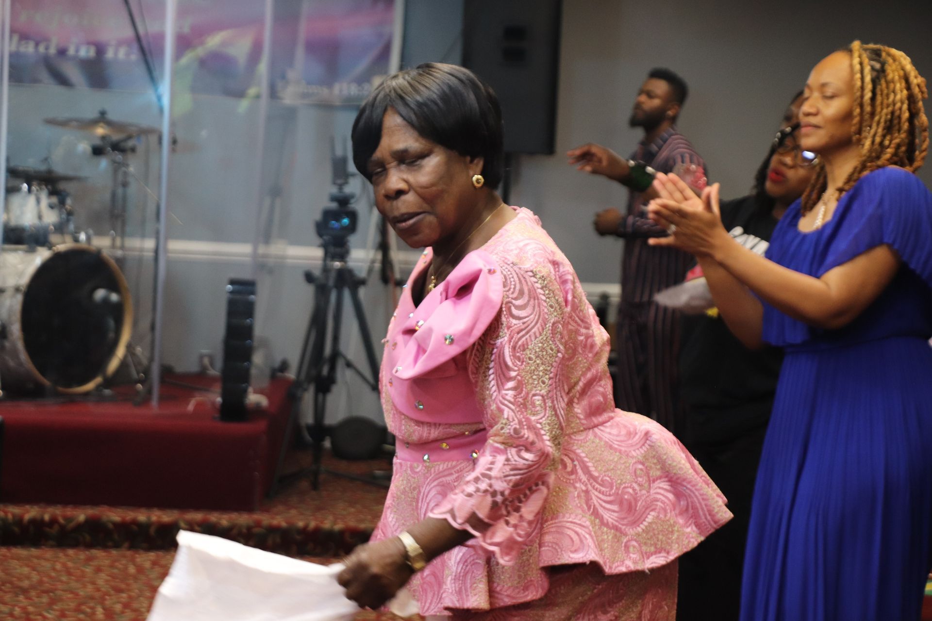 Woman in pink dress dances joyfully in church; others clap and sing.