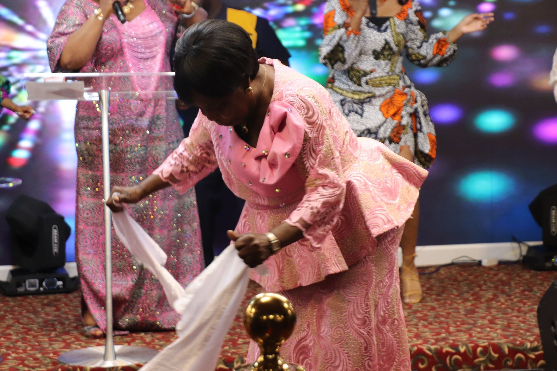 Woman in pink dress, bowing and holding white cloth on stage. Church service.