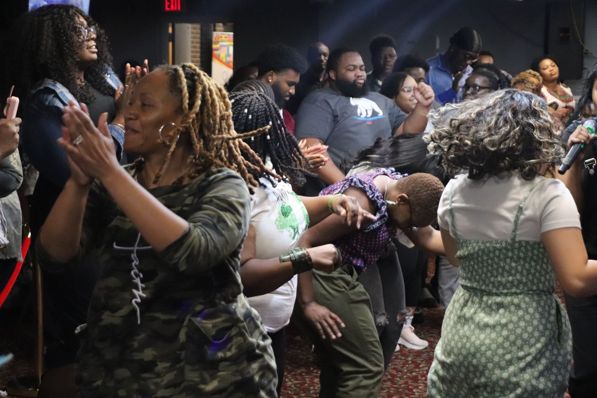 Group of people dancing and clapping in a dimly lit club. Some have their eyes closed, arms raised in the air.