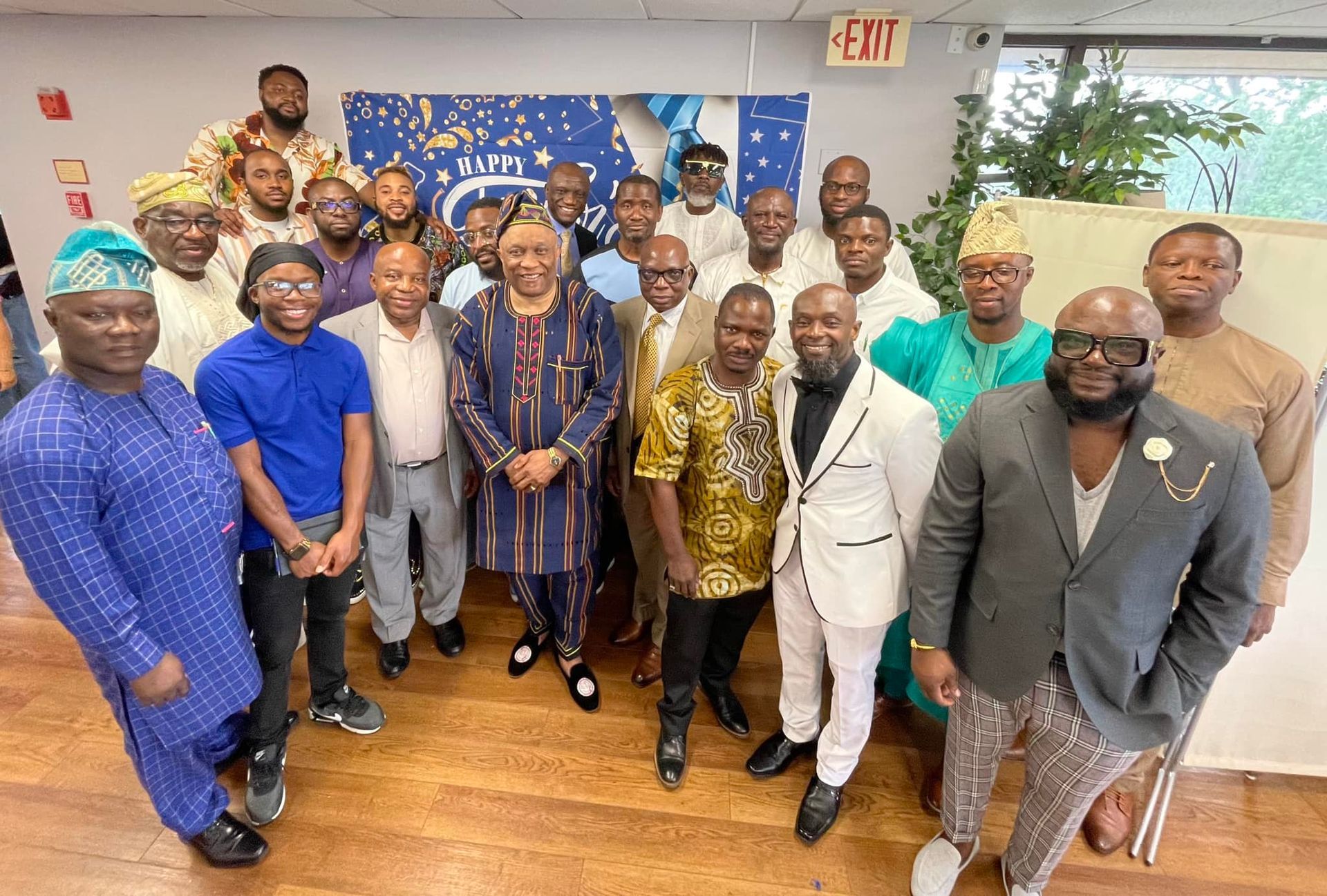 Group of men in traditional attire, smiling, gathered indoors for an event.