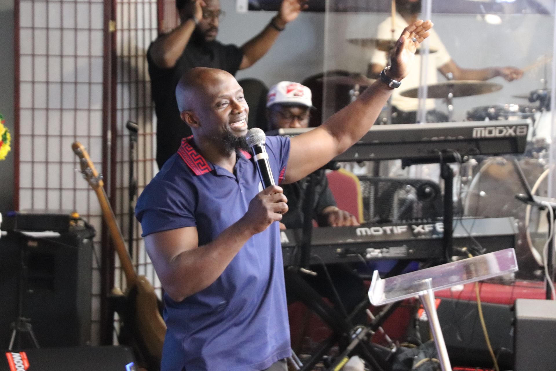 Man with microphone leading worship, arms raised, in front of band at church.