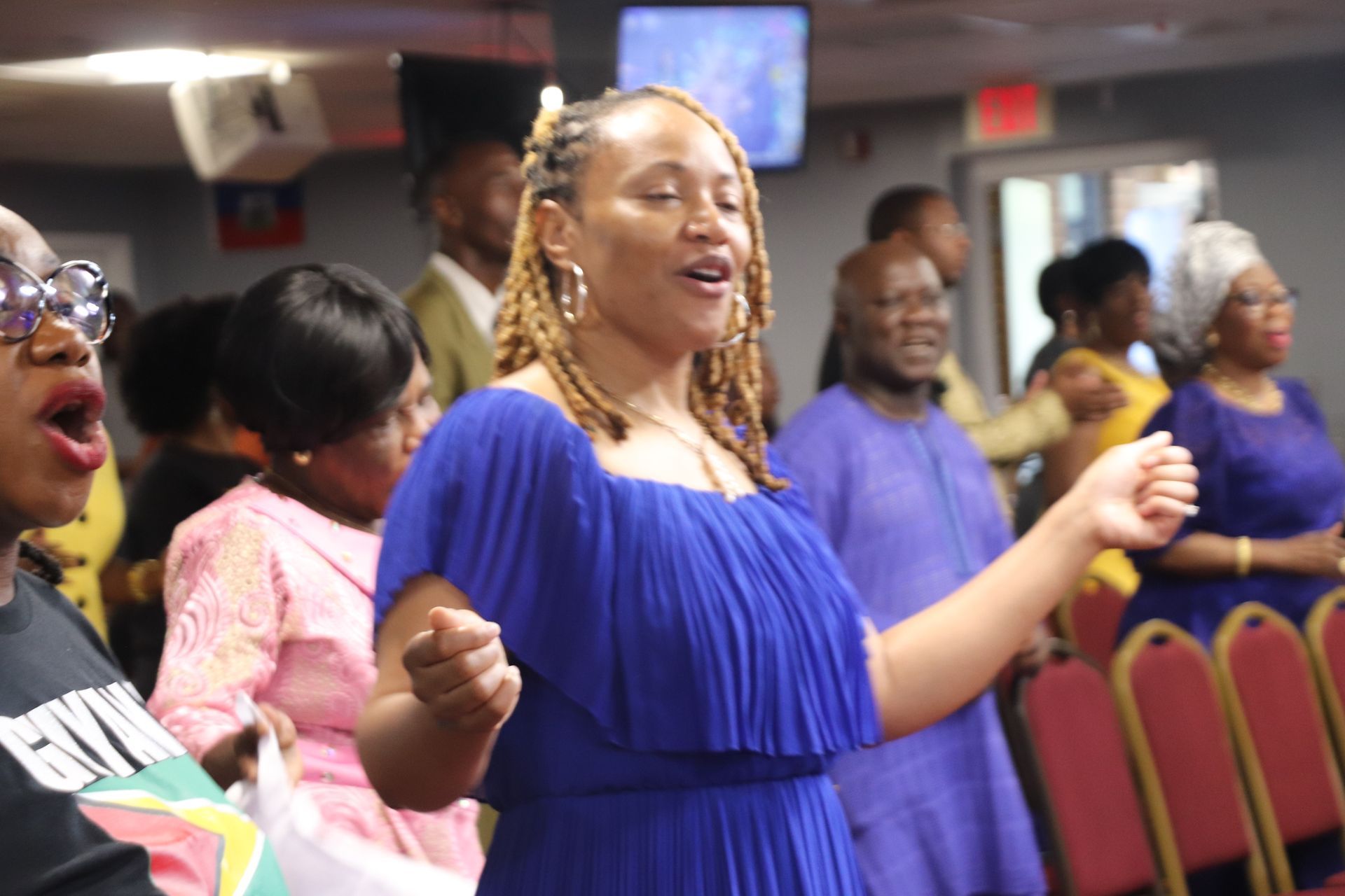 Woman in blue dress singing with eyes closed in a church. Others sing and lift hands.