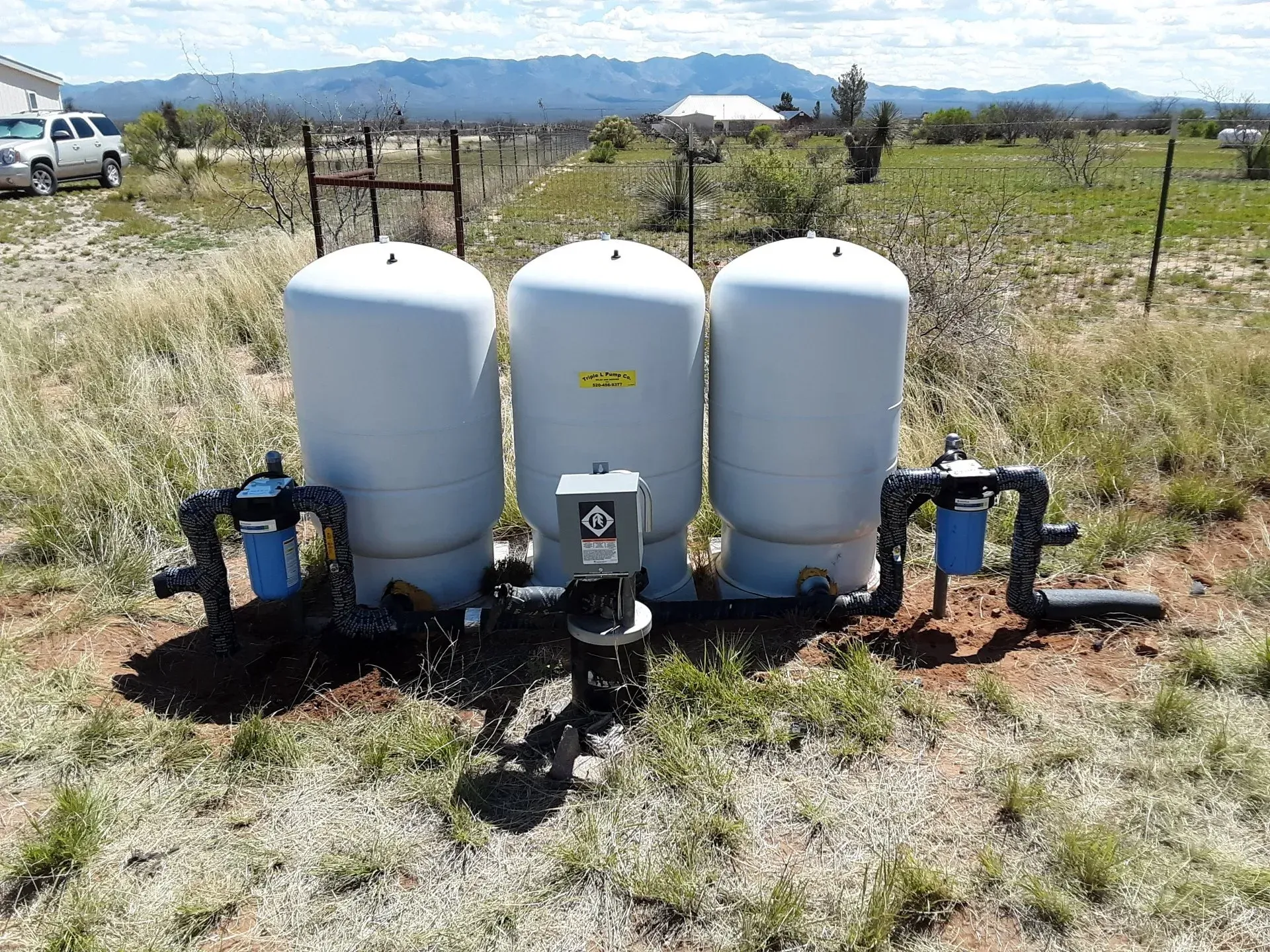 three water tanks are sitting in the middle of a grassy field .