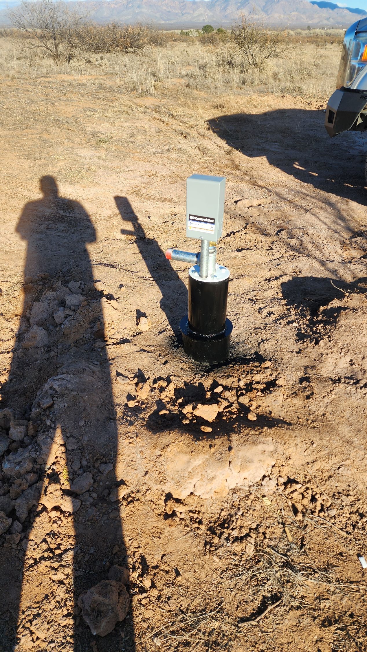 a shadow of a person is cast on the ground next to a well in the desert .